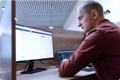 Blonde Man in Brown Red Shirt Sitting by Desk Looking at the Monitor